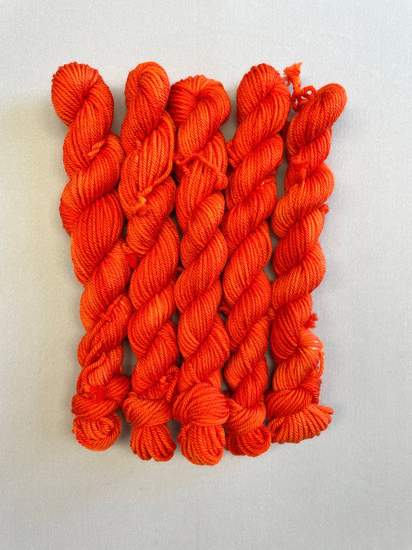 Zoomed in shot of DK weight mini skeins in colourway Lava. This semi-solid colourway is dyed up in a bright, intense orange. 