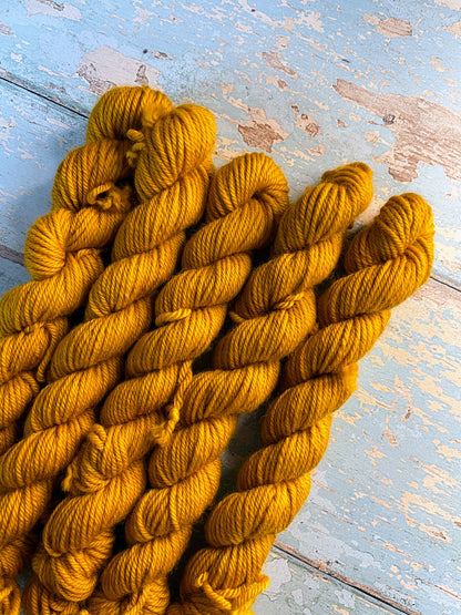 Close up shot of DK weight mini skeins in colourway Mustard. This is a semi-solid colourway in a rich, golden mustard colour.