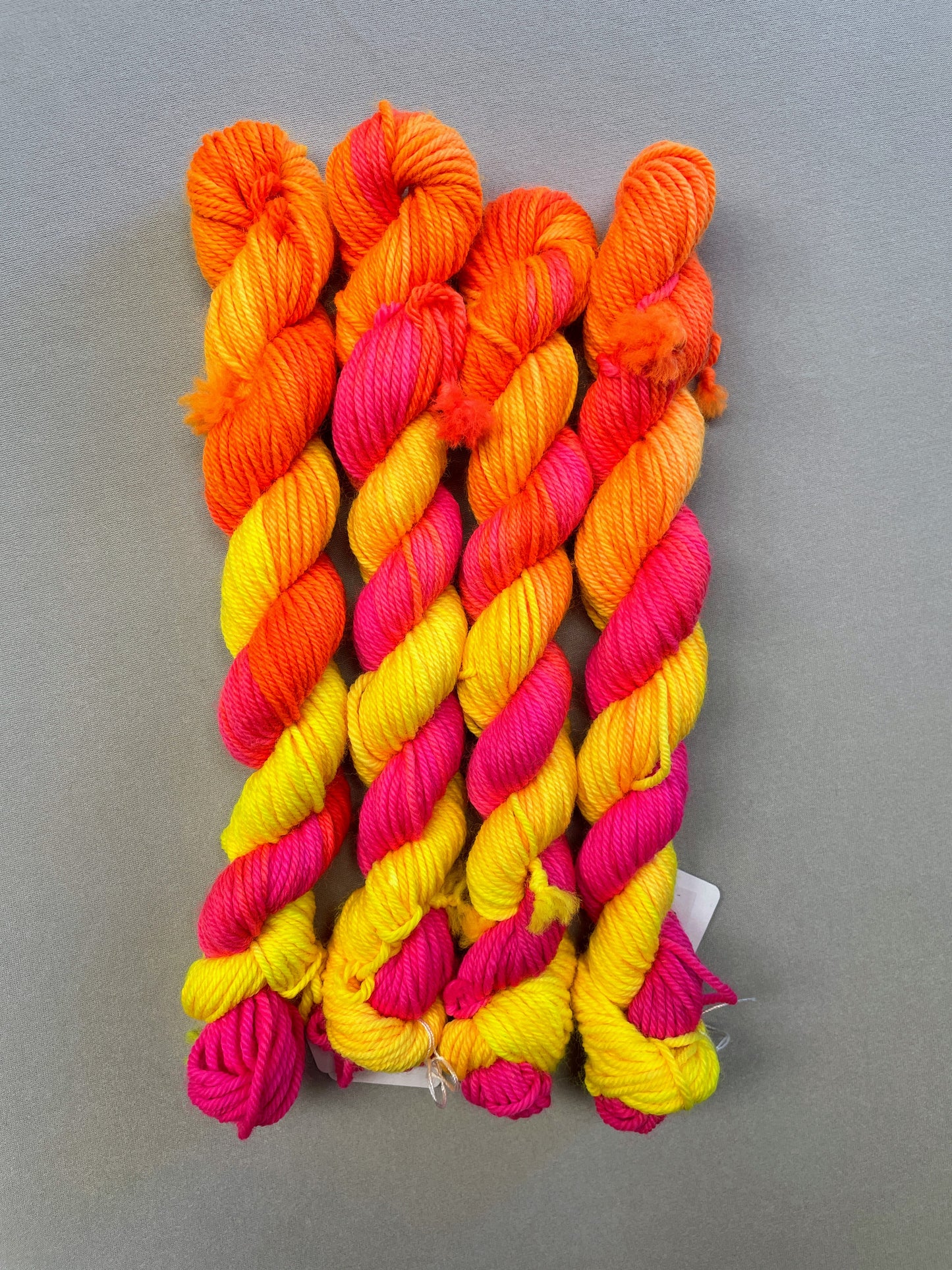 Full shot of 20g DK mini skeins in colourway Neon Funk. This colourway has three bands of colour in Neon Yellow, Neon Pink and Neon Orange. Photographed on a light grey background. 