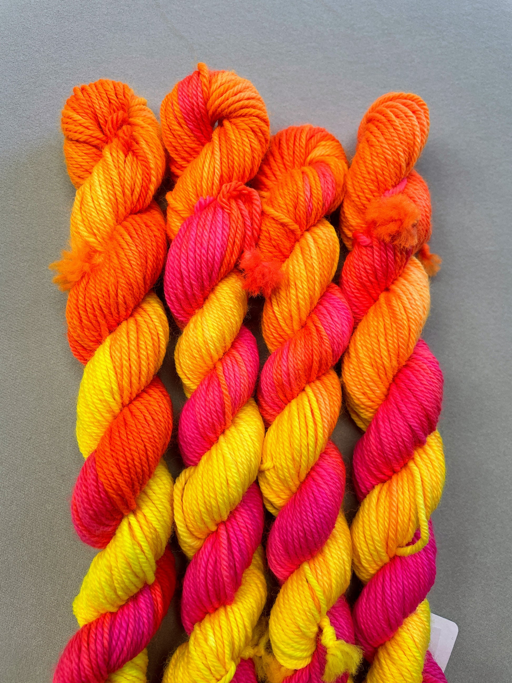 Zoomed in shot of 20g DK mini skeins in colourway Neon Funk. This colourway has three bands of colour in Neon Yellow, Neon Pink and Neon Orange. Photographed on a light grey background. 