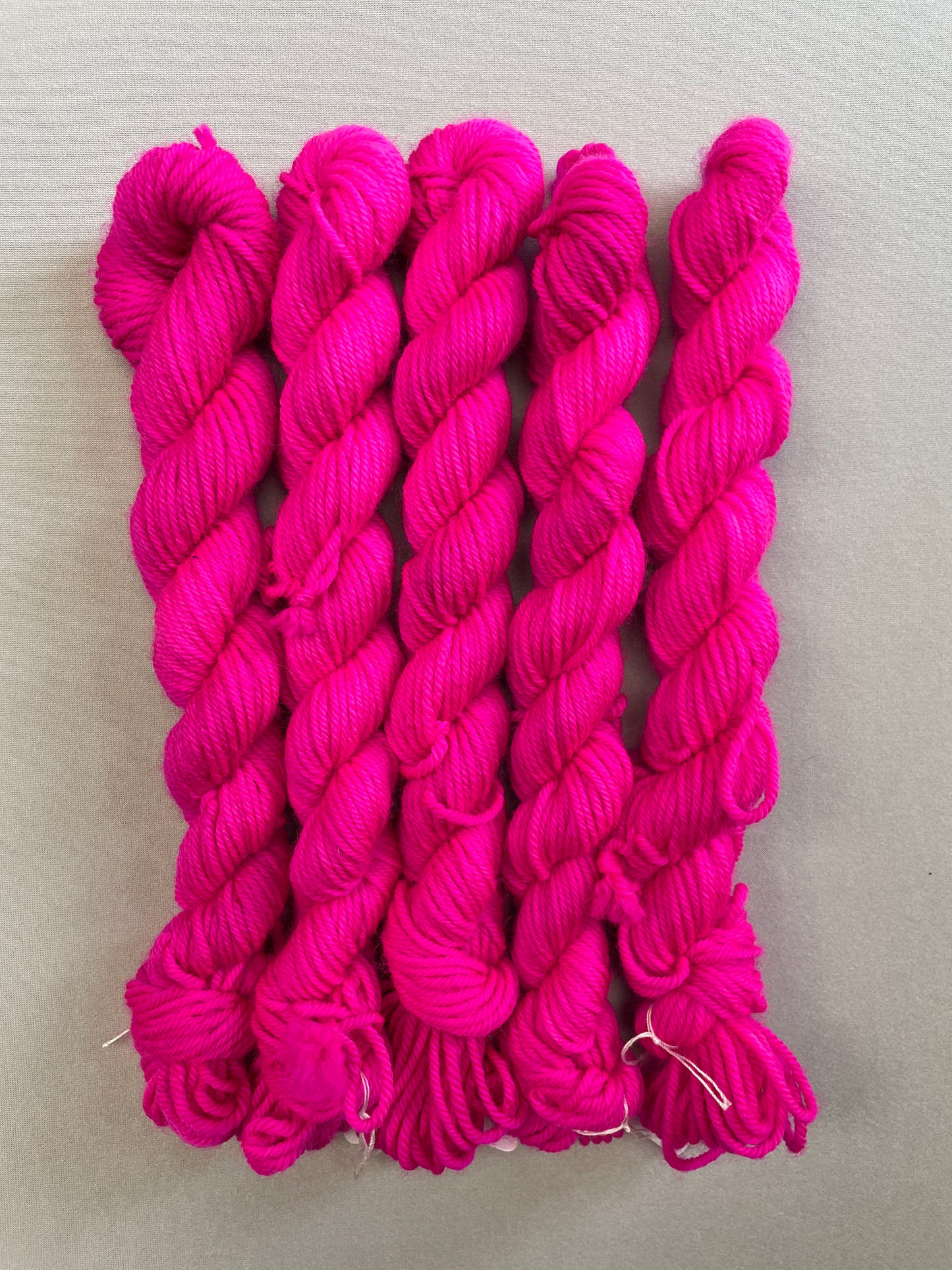 Full shot of 20g DK mini skeins in semi-solid colourway Neon Pink. This colourway glows under U.V. blue light and is as bright as a highlighter.