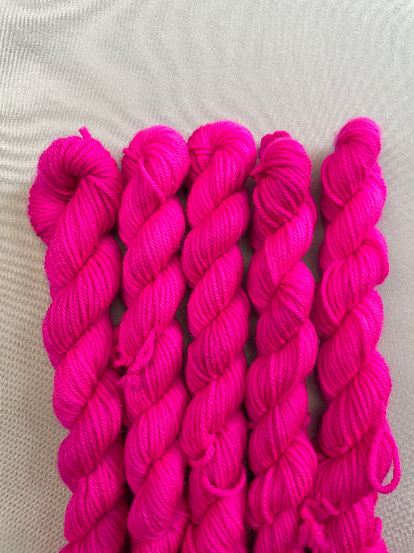 Zoomed in shot of 20g DK mini skeins in semi-solid colourway Neon Pink. This colourway glows under U.V. blue light and is as bright as a highlighter.