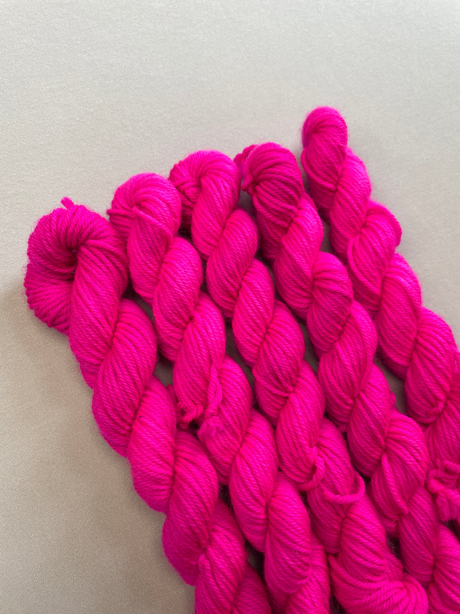 Close up shot of 20g DK mini skeins in semi-solid colourway Neon Pink. This colourway glows under U.V. blue light and is as bright as a highlighter.