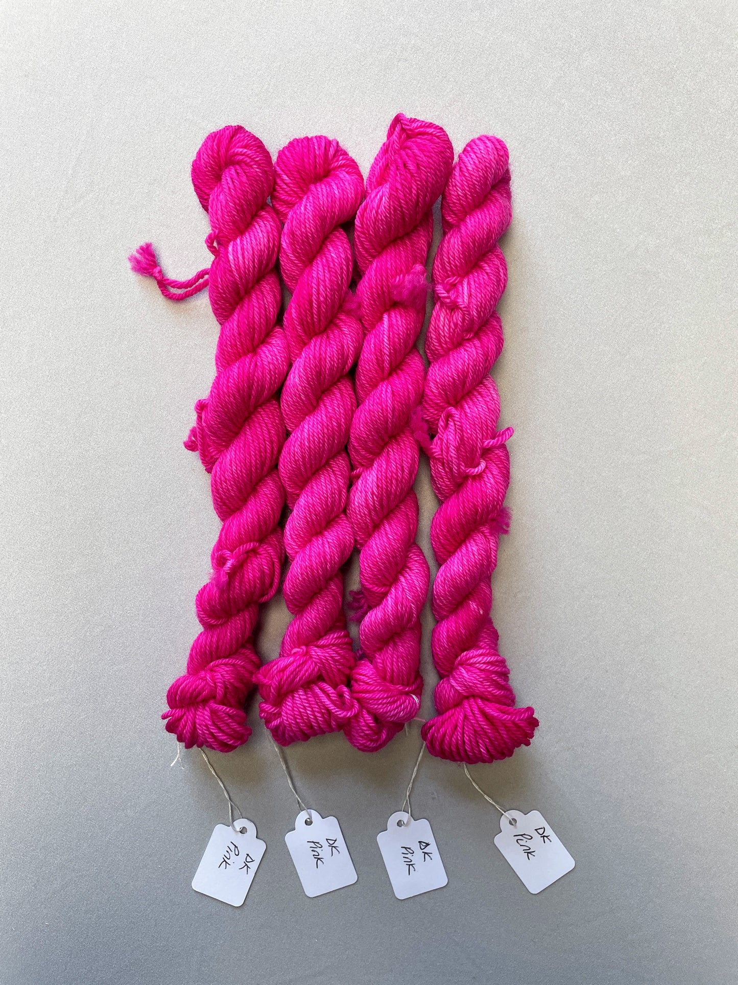 Full shot of 20g DK weight mini skeins in colourway Pink. A semi-solid colourway in a bright pink shade. 