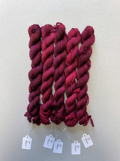 Full shot of 20g DK weight mini skeins in semi-solid colourway Plum an intense, deep Plum/Burgundy. Photographed on a light grey background.