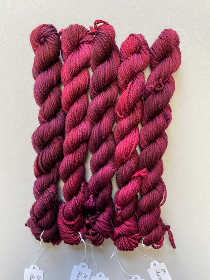 Zoomed in shot of 20g DK weight mini skeins in semi-solid colourway Plum an intense, deep Plum/Burgundy. Photographed on a light grey background.