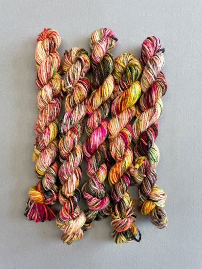 Full shot of 20g DK mini skeins in colourway Punk Rocker. An undyed yarn base with layers of Neon sprinkles in Yellow, Pink, Green and Black. This colourway glows under U.V. light. 