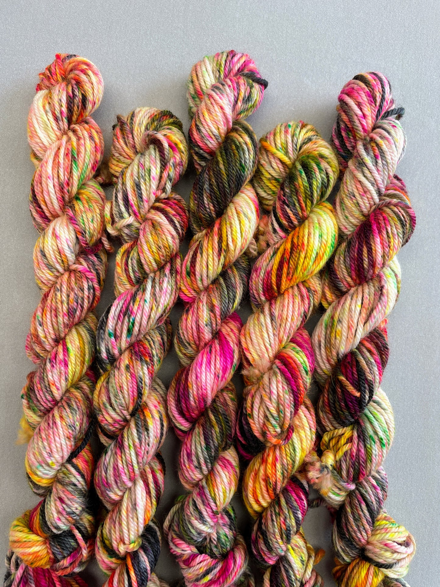 Zoomed in shot of 20g DK mini skeins in colourway Punk Rocker. An undyed yarn base with layers of Neon sprinkles in Yellow, Pink, Green and Black. This colourway glows under U.V. light. 