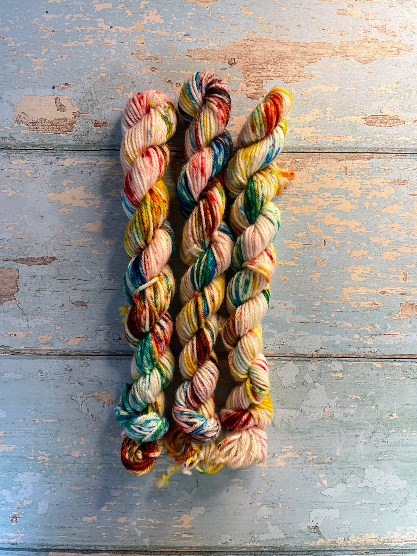 Full shot of 20g DK weight mini skeins in colourway Rainbow Sprinkles. This is an undeyd yarn base with layers of speckles in red, yellow, green, blue. 