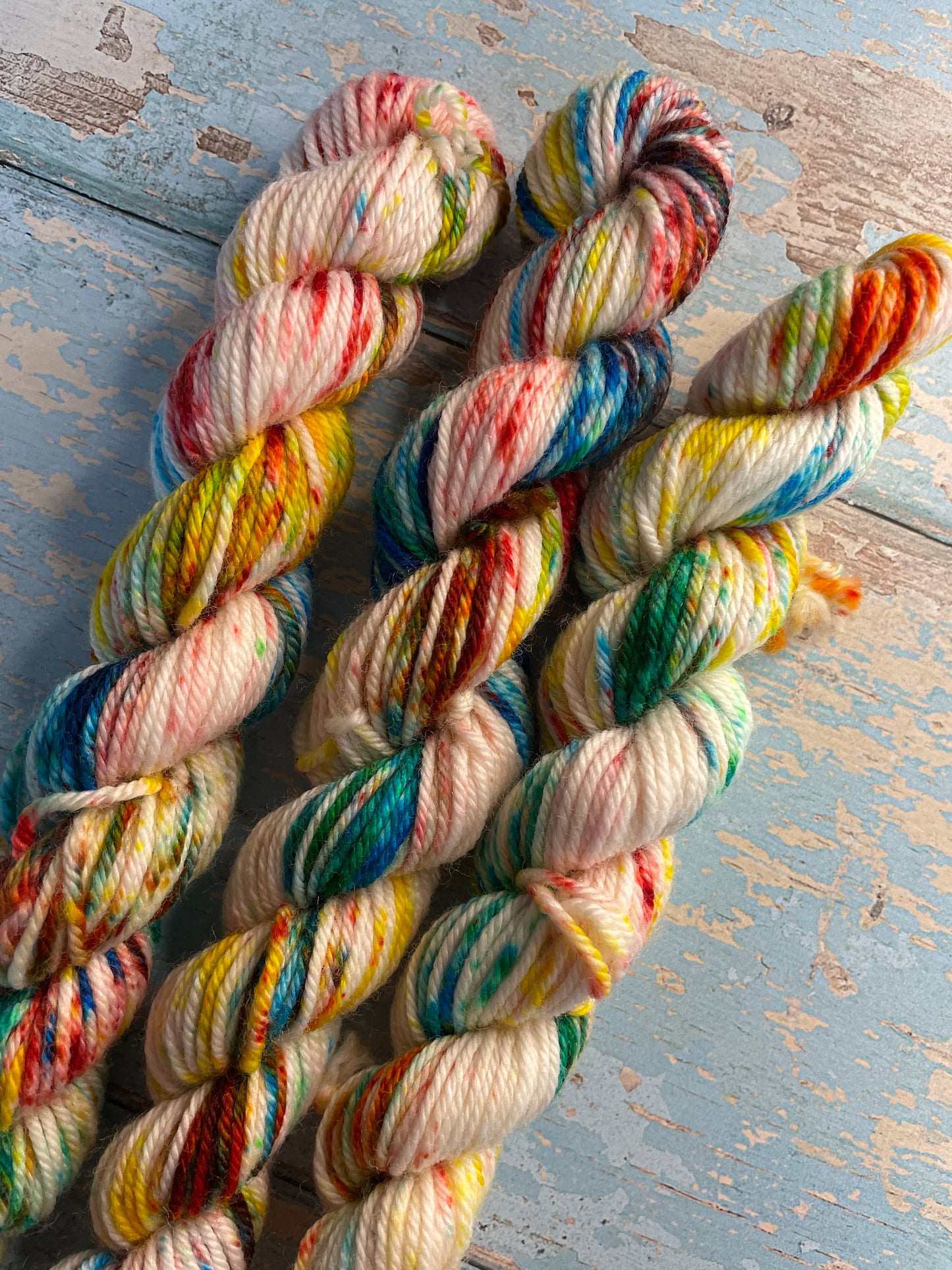 Close up shot of 20g DK weight mini skeins in colourway Rainbow Sprinkles. This is an undeyd yarn base with layers of speckles in red, yellow, green, blue. 