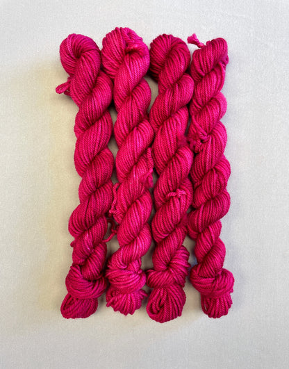 Zoomed in shot of 20g DK weight mini skeins in semi-solid colourway Raspberry, an intense, deep pink. Photographed on a light grey background.