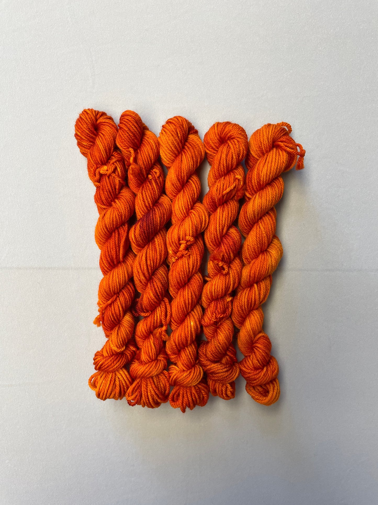 Full shot of 20g DK weight mini skeins in semi-solid colourway Saffron, a deep and intense orange colourway.