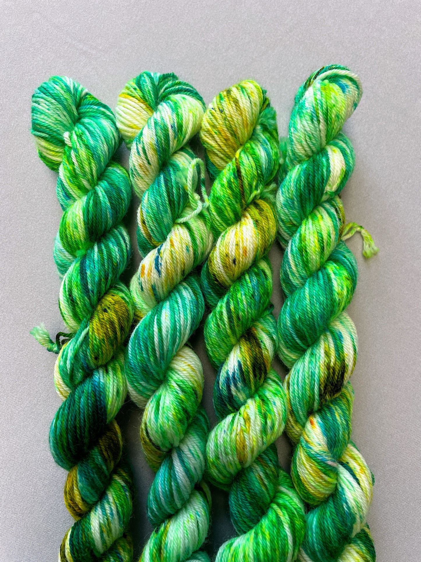 Up close shot of 20g sock weight mini skein in colourway Apple Sprinkles. Shows the close up definition of the green speckles in shades Emerald, Olive Green and Neon Green. 