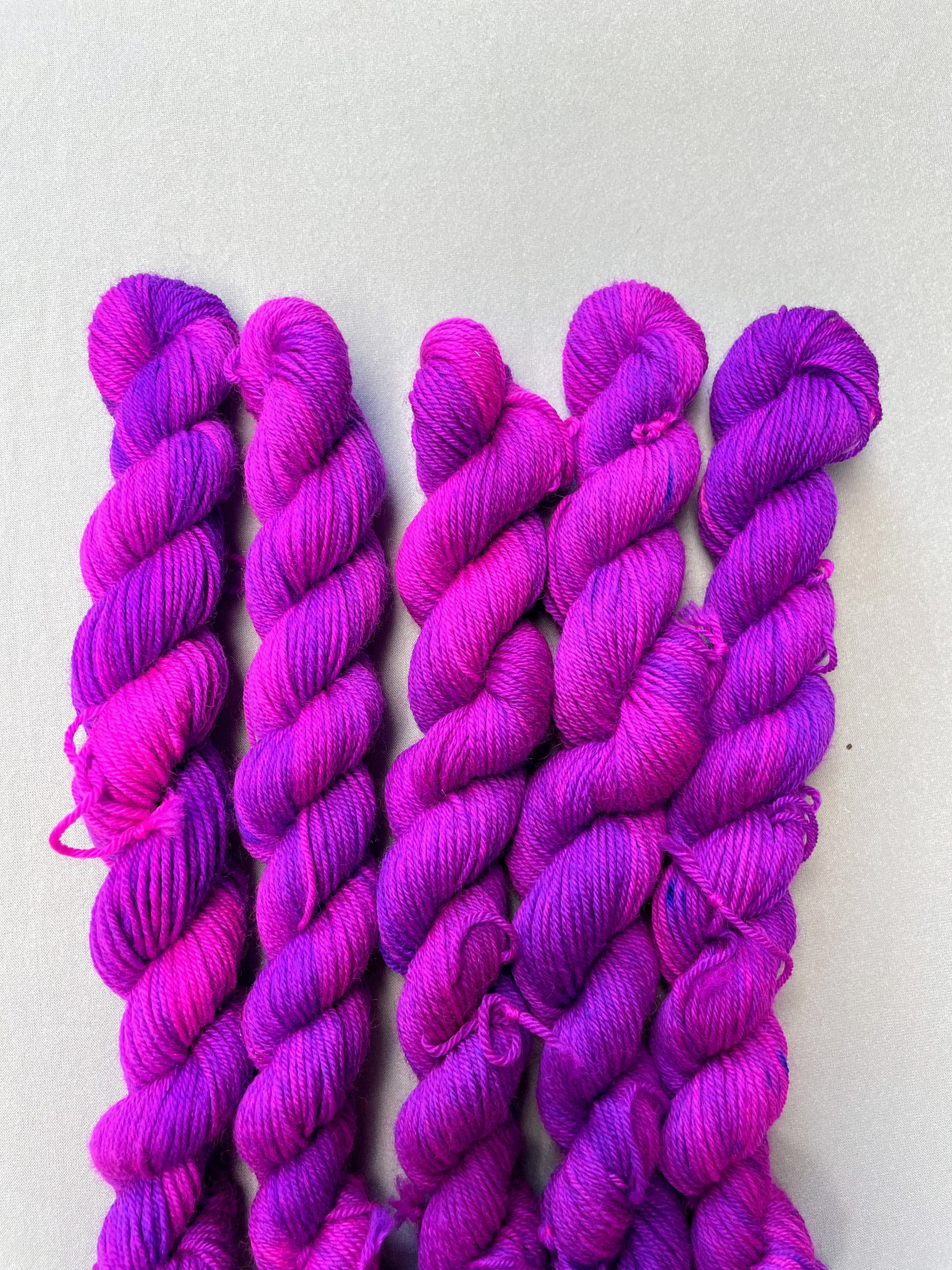 Zoomed in shot of 20g Sock weigh mini skeins in colourway Electric Purple. This colourway is an intense and bright purple that breaks into Neon Pink. Photographed on light grey background.