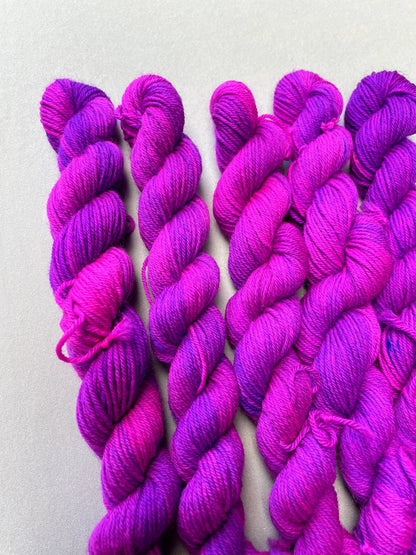 Close up shot of 20g Sock weigh mini skeins in colourway Electric Purple. This colourway is an intense and bright purple that breaks into Neon Pink. Photographed on light grey background.