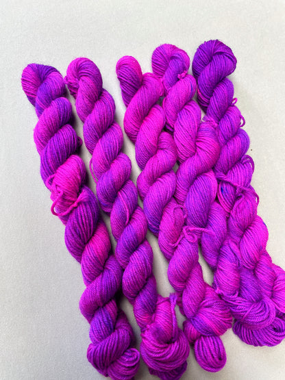 Angled shot of 20g Sock weigh mini skeins in colourway Electric Purple. This colourway is an intense and bright purple that breaks into Neon Pink. Photographed on light grey background.