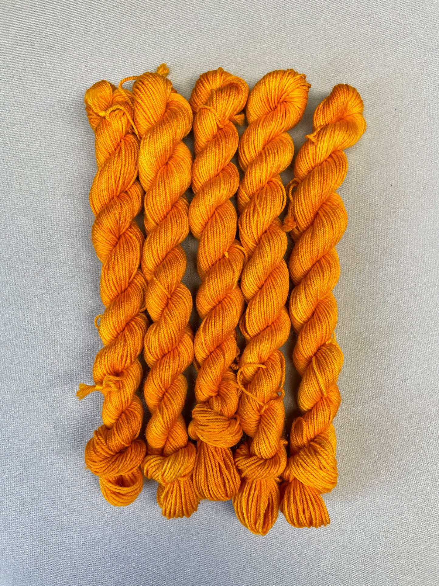 5 x 20g twisted, Sock mini skeins in colourway Golden Poppy, photographed on light grey background. Golden Poppy is a semi-solid colourway in a golden, yellow tone. 