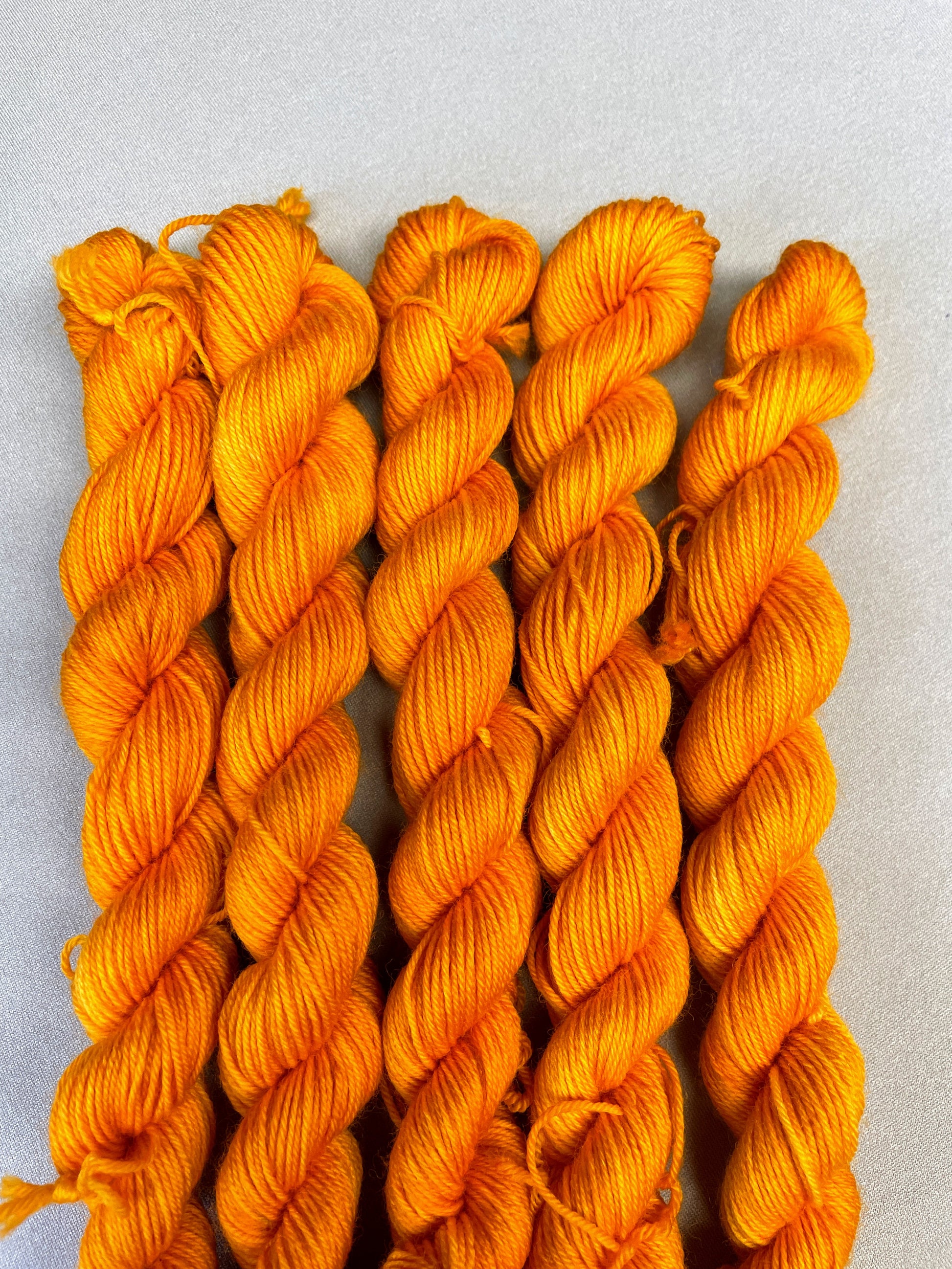 5 x 20g twisted, Sock mini skeins in colourway Golden Poppy, photographed on light grey background. Golden Poppy is a semi-solid colourway in a golden, yellow tone. 