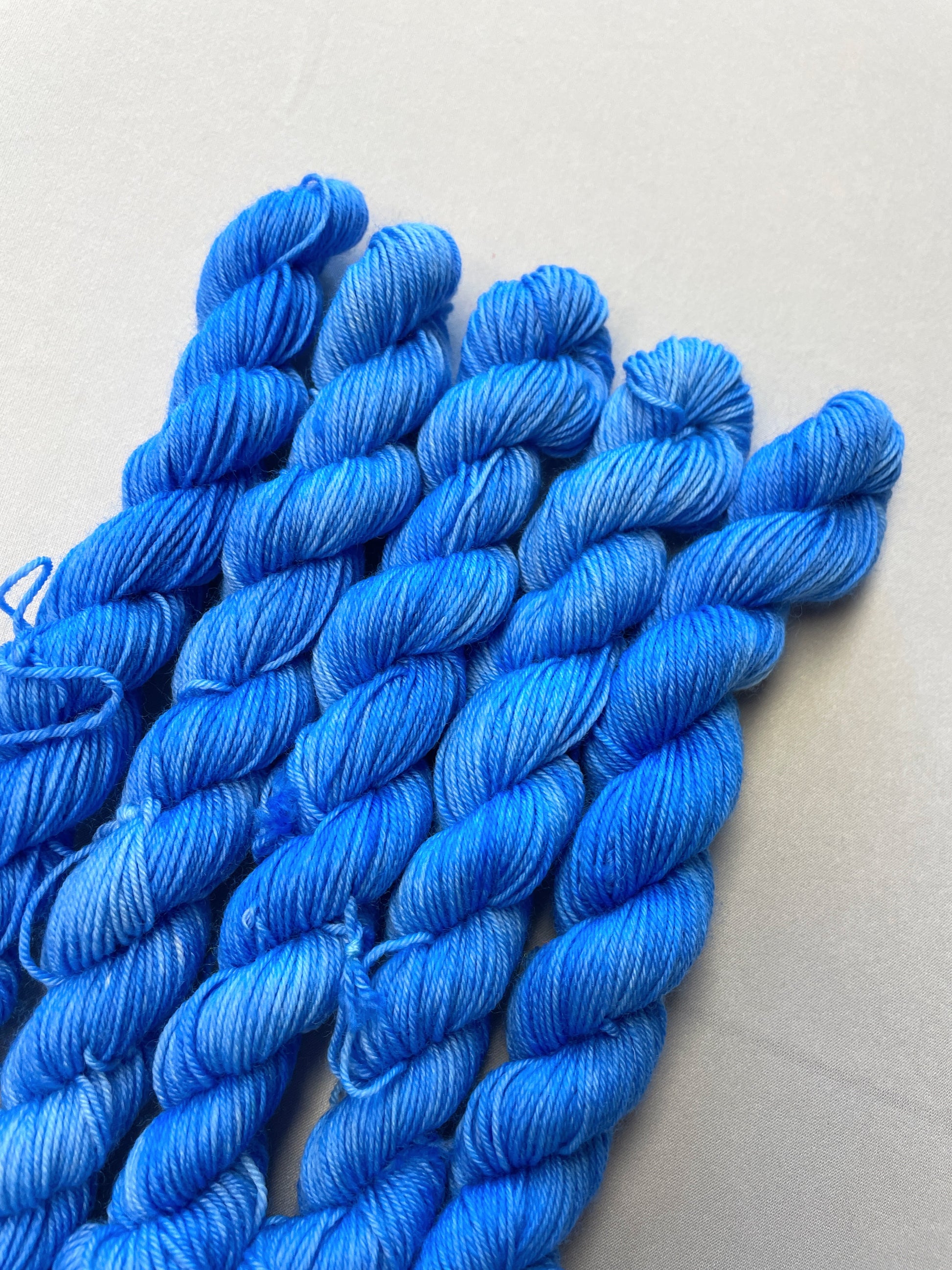 Close up shot of 20g sock weight mini skeins in the semi-solid colourway Intense Blue. This colourway is a light blue colour. 