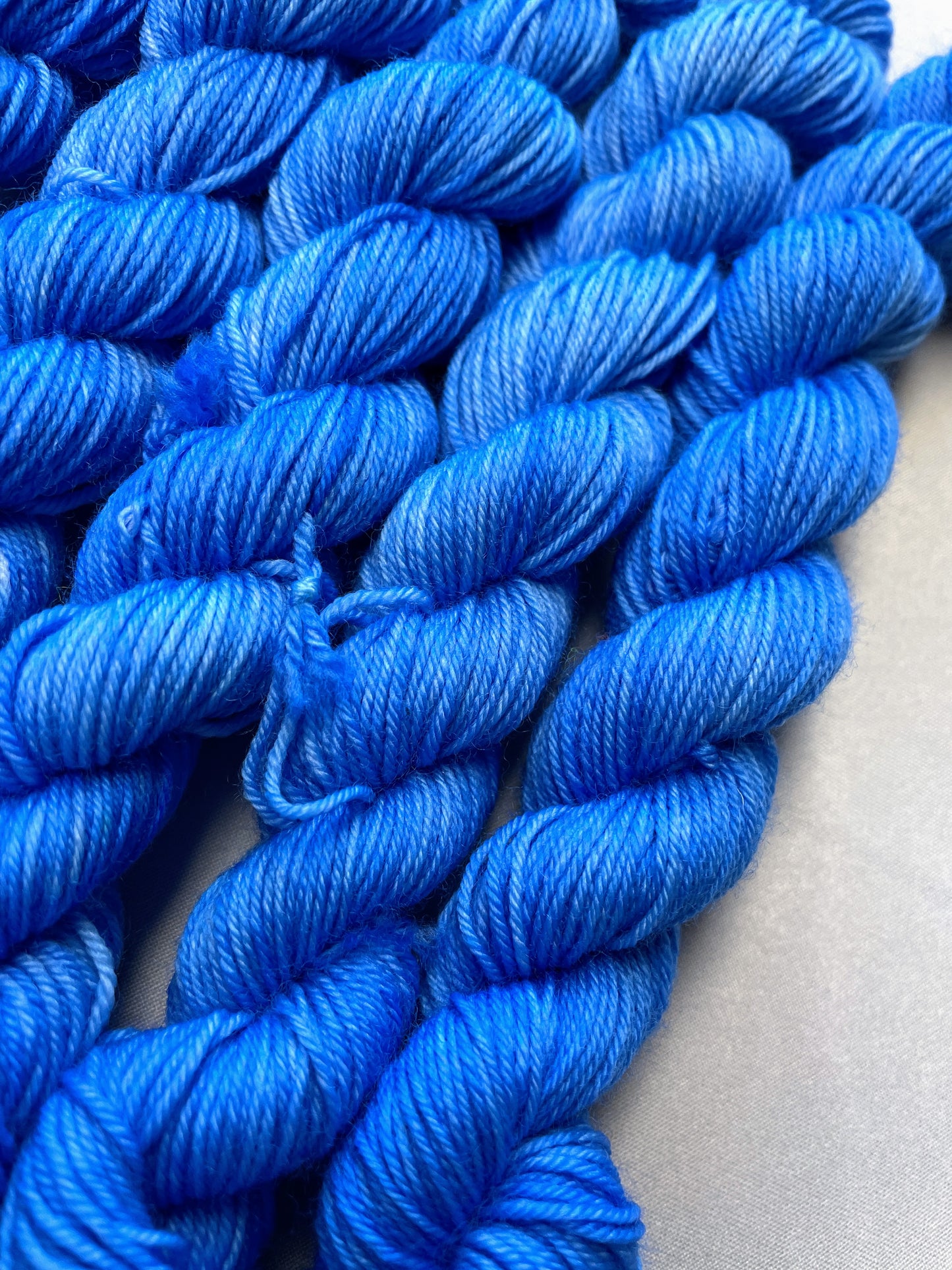 Close up shot of 20g sock weight mini skeins in the semi-solid colourway Intense Blue. This colourway is a light blue colour. 