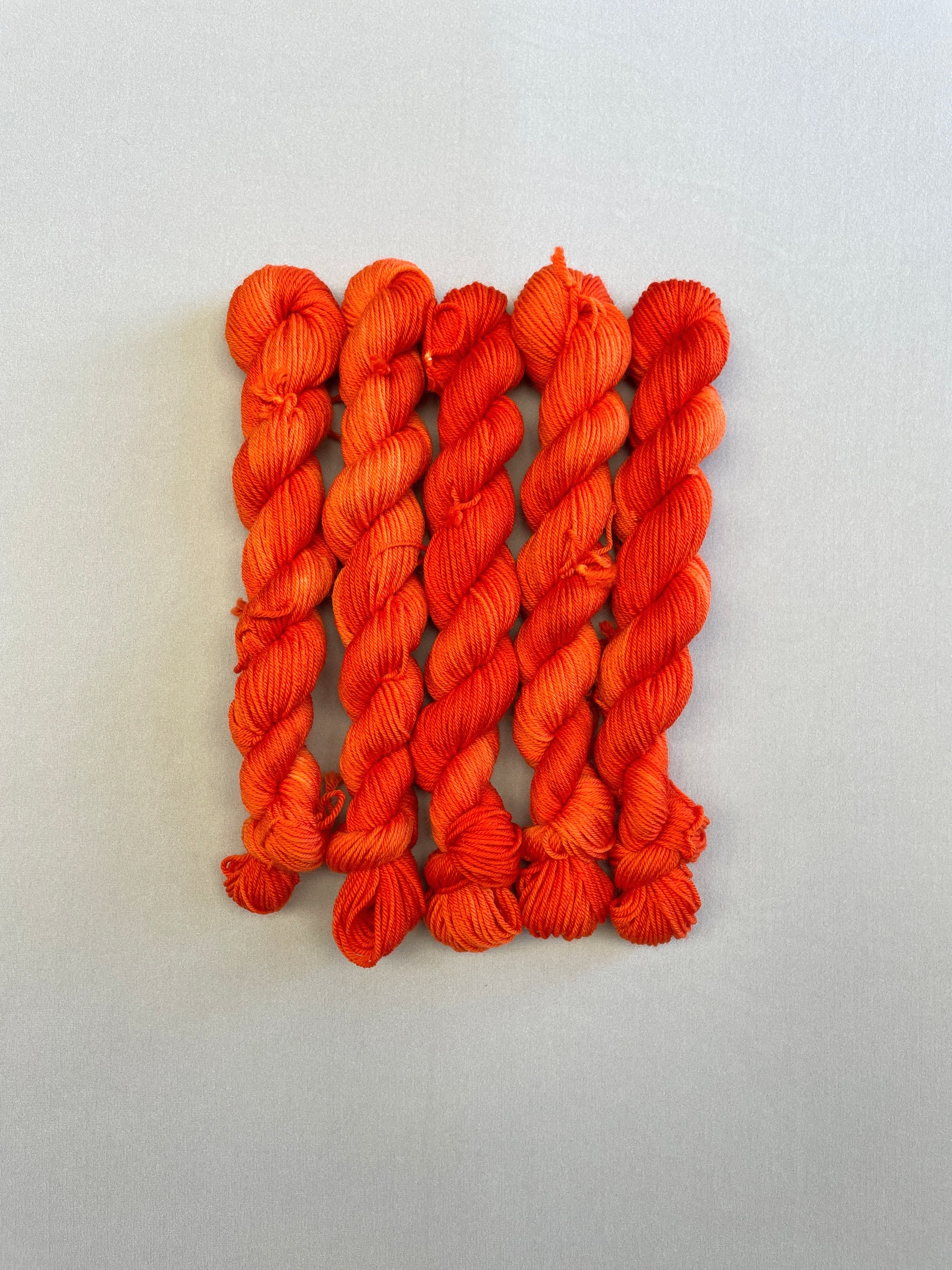 Full shot of Sock weight mini skeins in colourway Lava. This semi-solid colourway is dyed up in a bright, intense orange. 