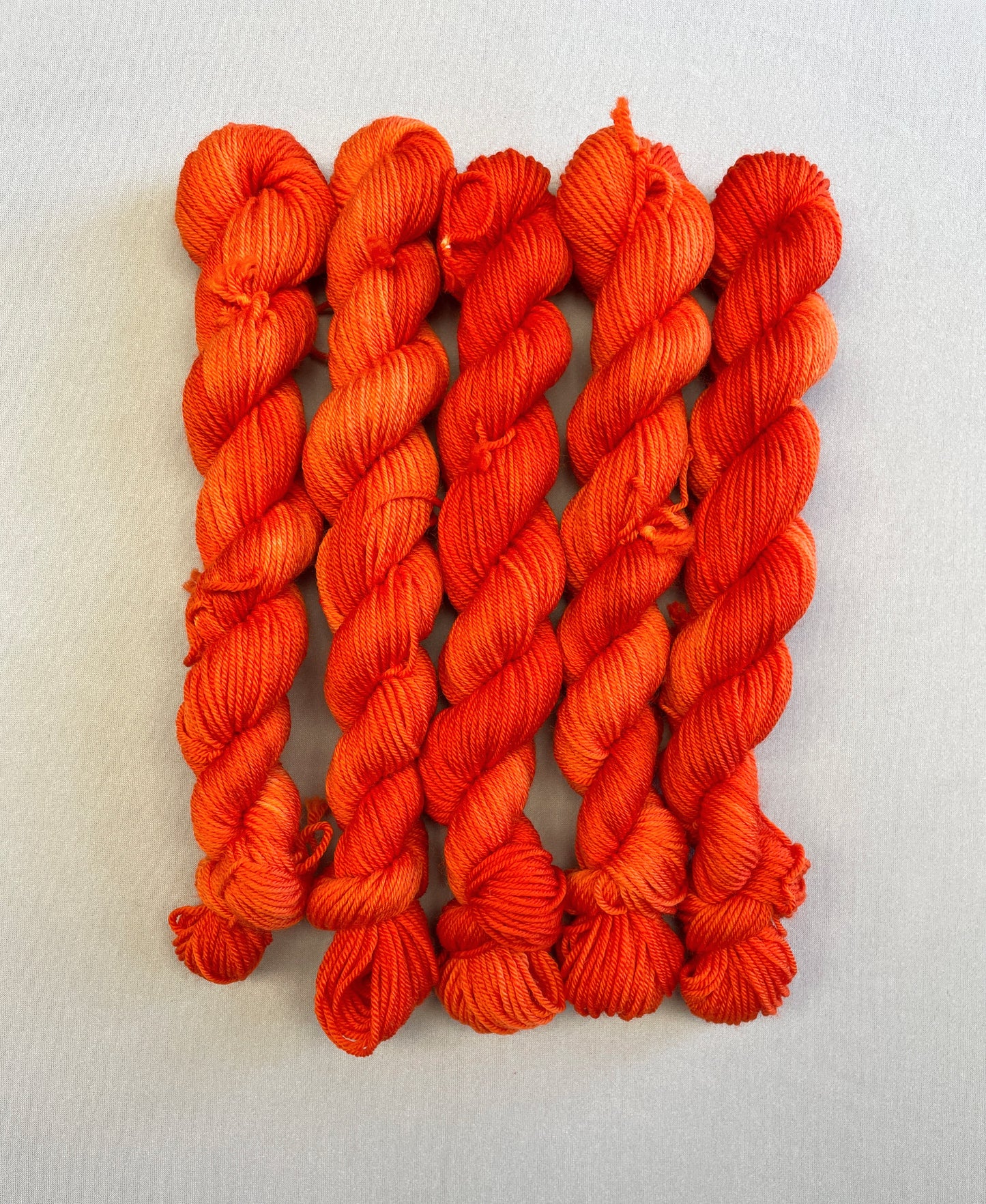 Zoomed in shot of Sock weight mini skeins in colourway Lava. This semi-solid colourway is dyed up in a bright, intense orange. 