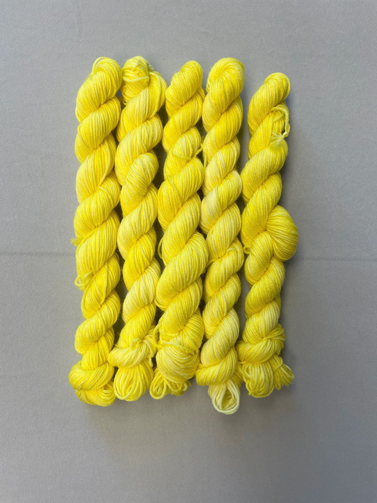 Zoomed in shot of 20g Sock weight mini skeins in colourway Lemon. A semi-solid colourway of pale yellow colour. 