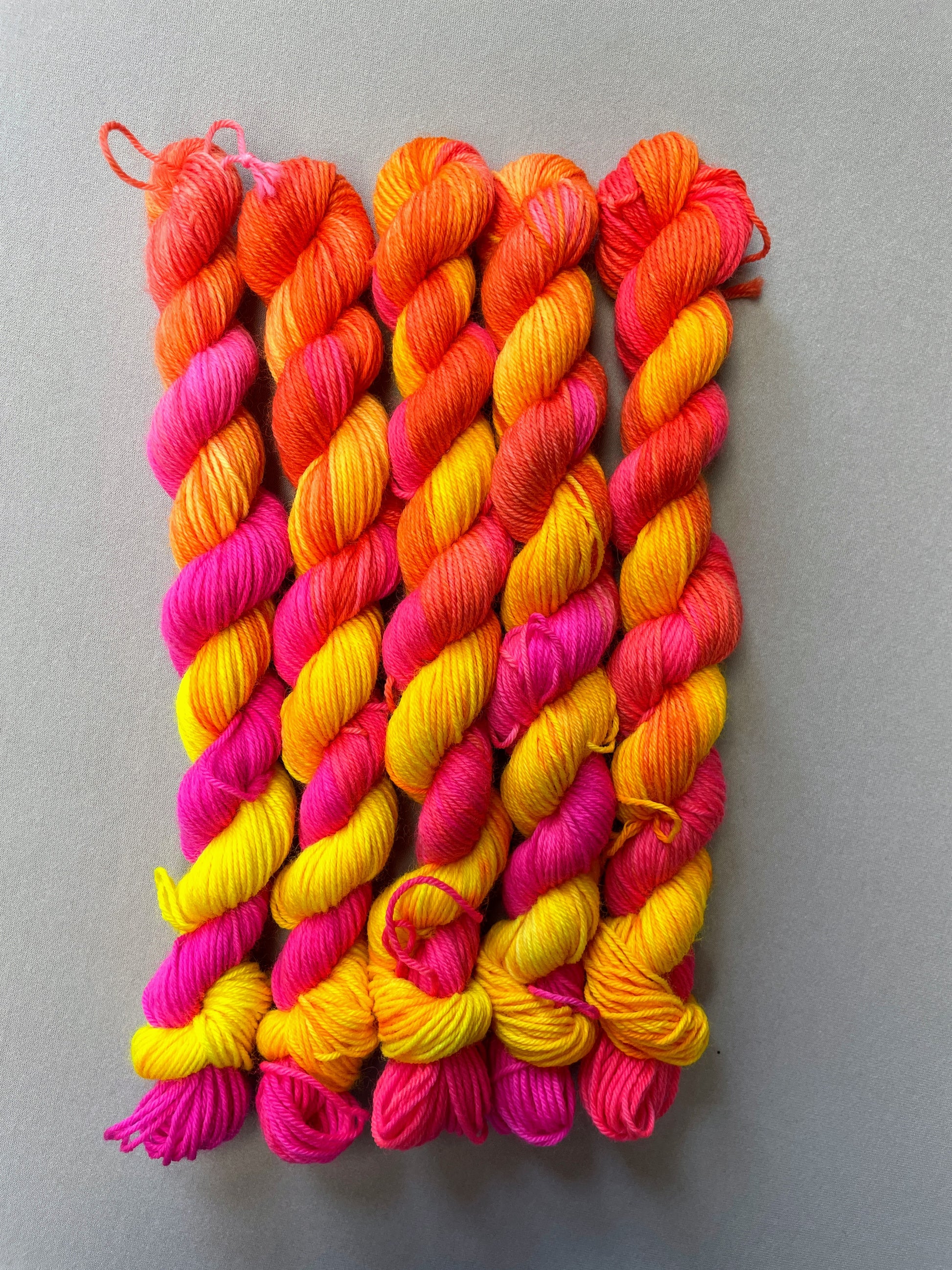 Full shot of 20g sock mini skeins in colourway Neon Funk. This colourway has three bands of colour in Neon Yellow, Neon Pink and Neon Orange. Photographed on a light grey background. 