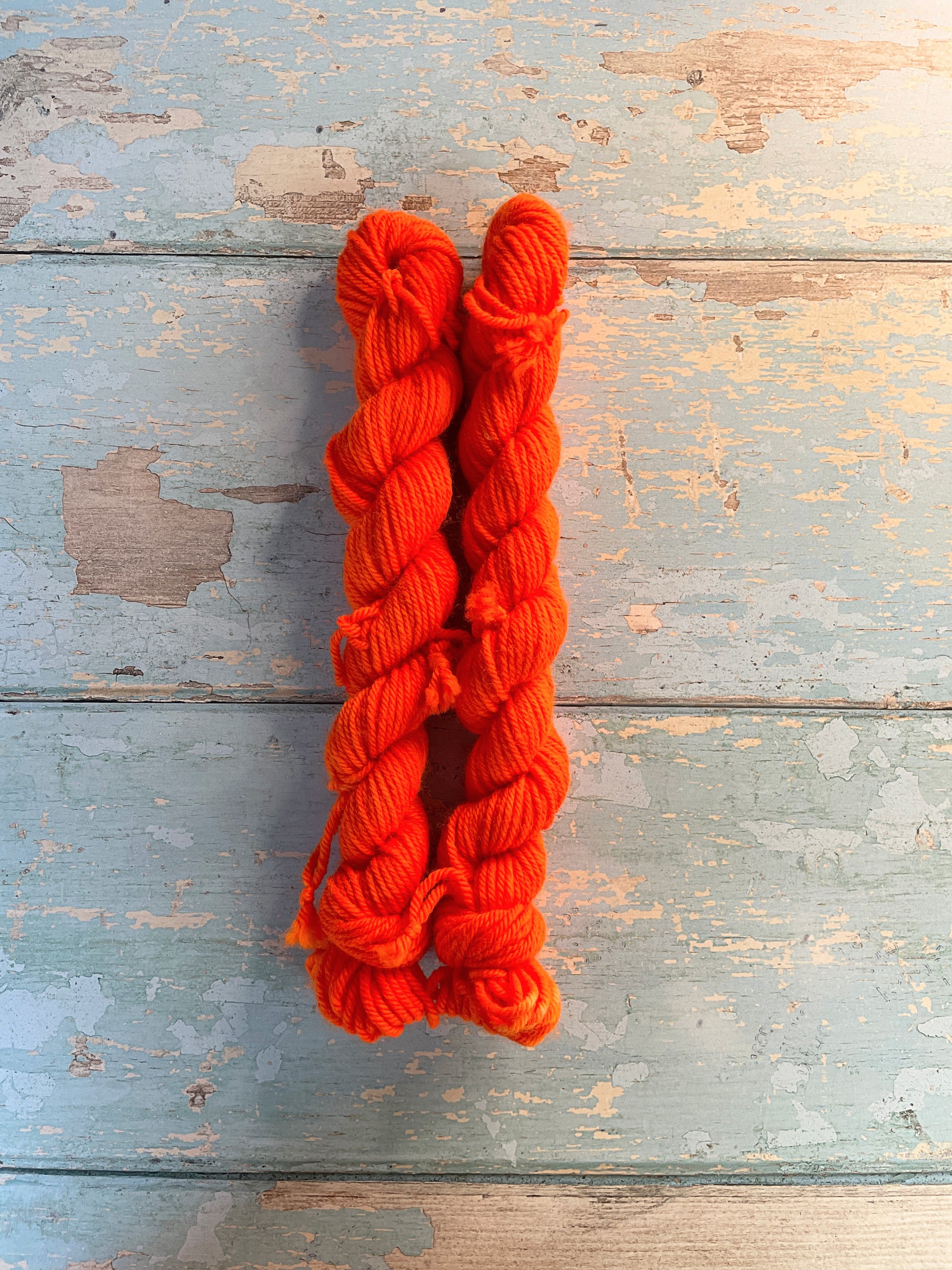 Full shot of 20g sock weight mini skeins in semi-solid colourway Neon Orange. An intense orange that shines under U.V. light.