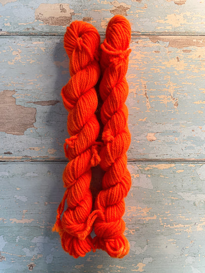 Zoomed in shot of 20g sock weight mini skeins in semi-solid colourway Neon Orange. An intense orange that shines under U.V. light.