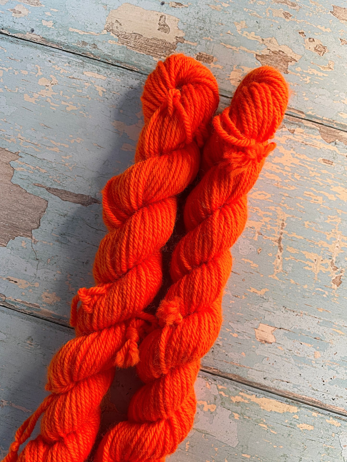 Close up shot of 20g sock weight mini skeins in semi-solid colourway Neon Orange. An intense orange that shines under U.V. light.