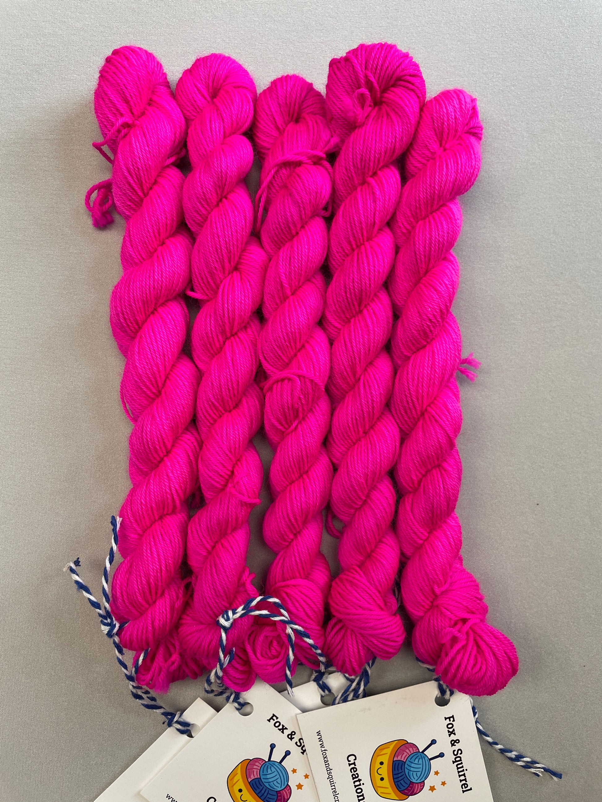 Full shot of 20g sock mini skeins in semi-solid colourway Neon Pink. This colourway glows under U.V. blue light and is as bright as a highlighter.