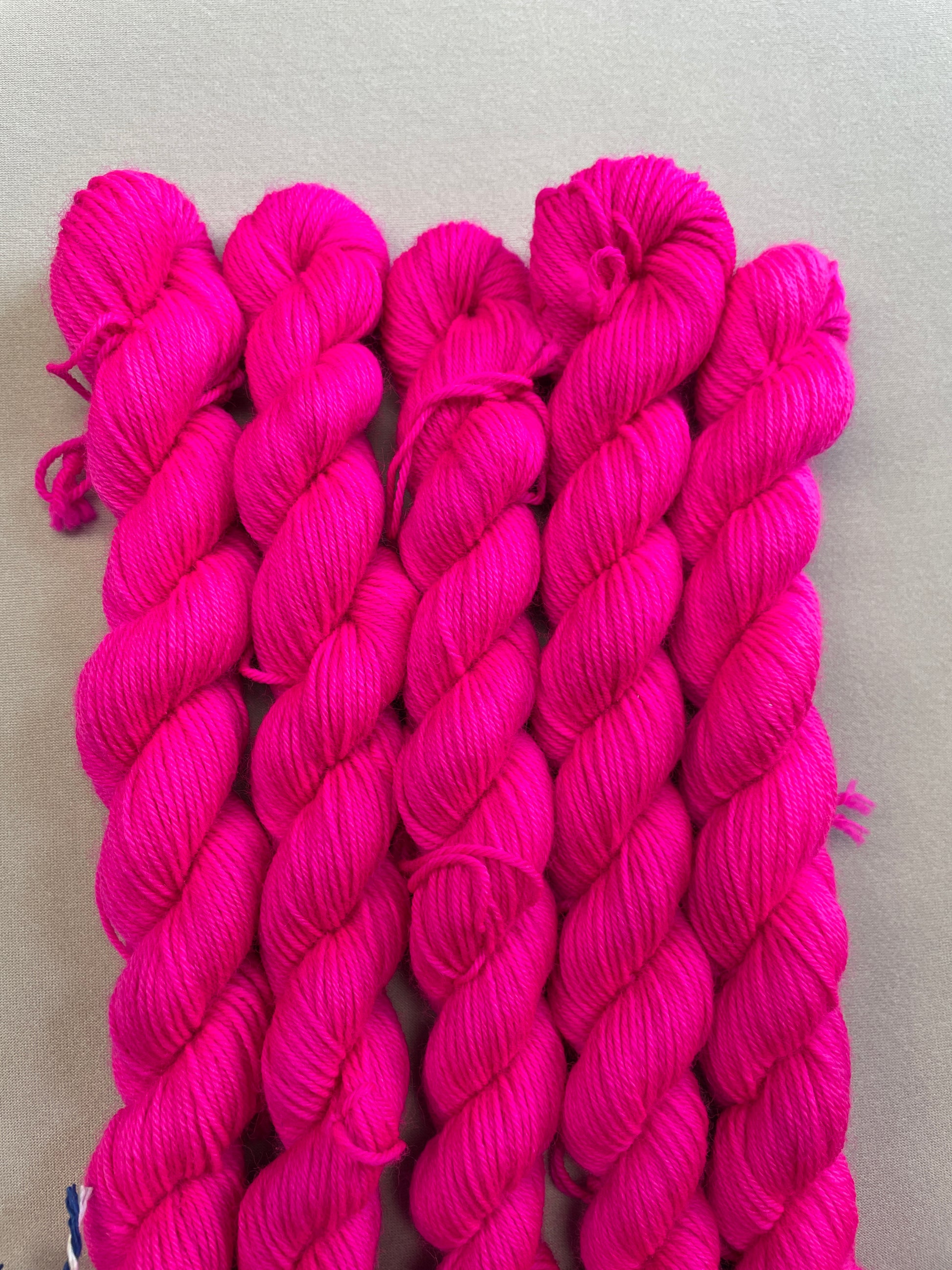 Zoomed in shot of 20g sock mini skeins in semi-solid colourway Neon Pink. This colourway glows under U.V. blue light and is as bright as a highlighter.