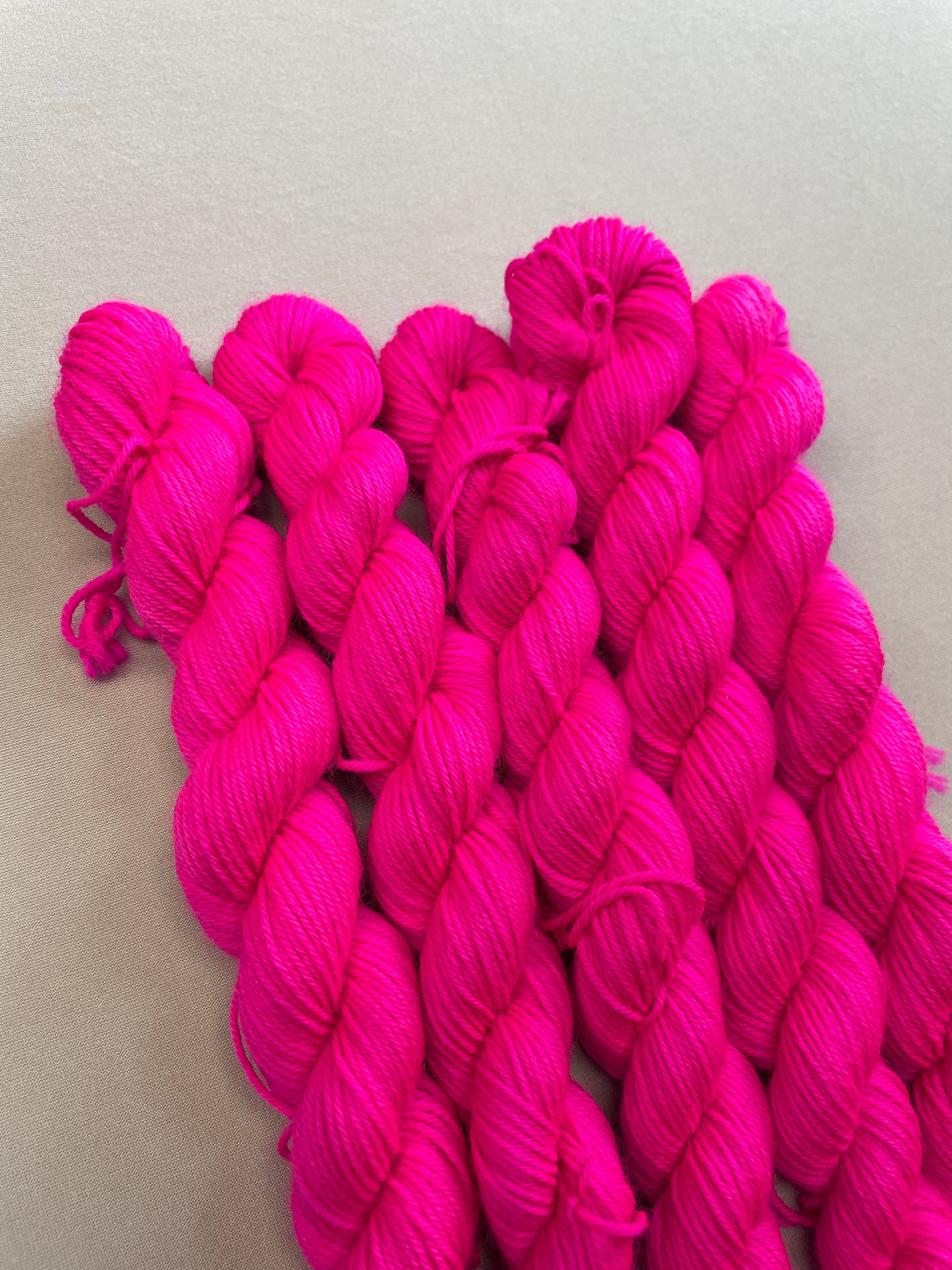 Close up shot of 20g sock mini skeins in semi-solid colourway Neon Pink. This colourway glows under U.V. blue light and is as bright as a highlighter.