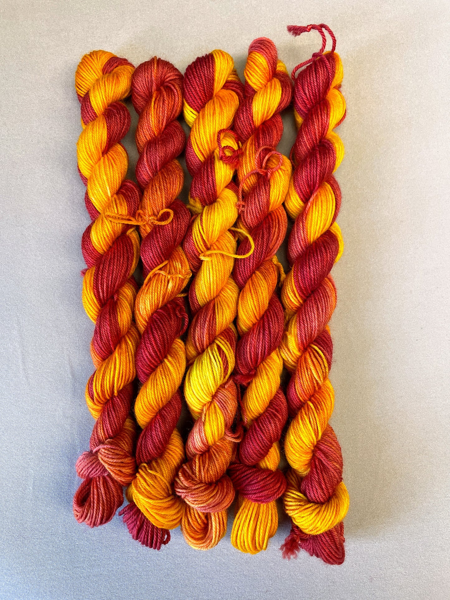 Hand-dyed Yarn
5 x 20g twisted, Sock mini skeins in colourway Phoenix, photographed on light grey background. This colourway is full of tones of Golden Poppy, Ruby Red and Saffron.