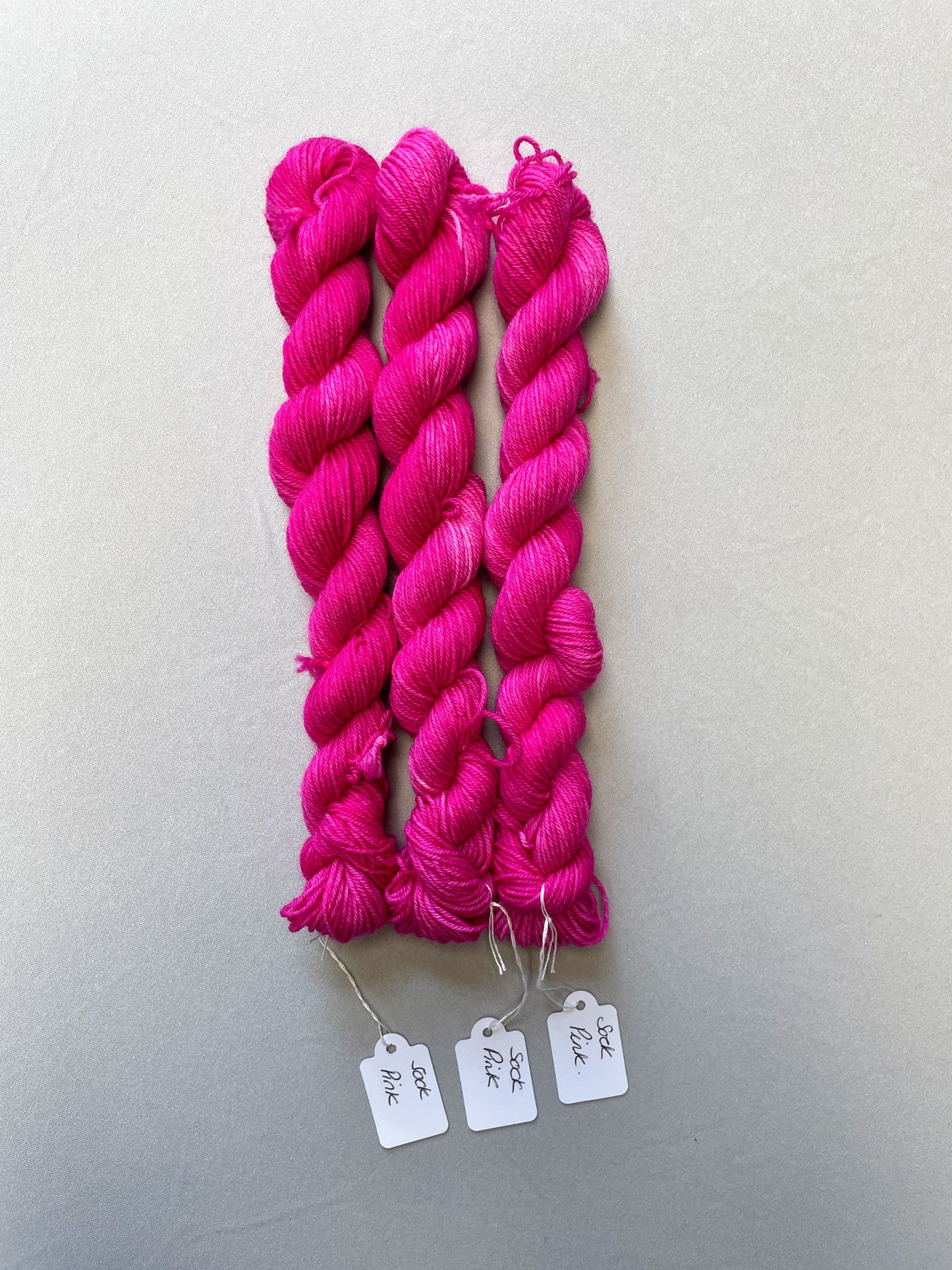 Full shot of 20g sock weight mini skeins in colourway Pink. A semi-solid colourway in a bright pink shade. 