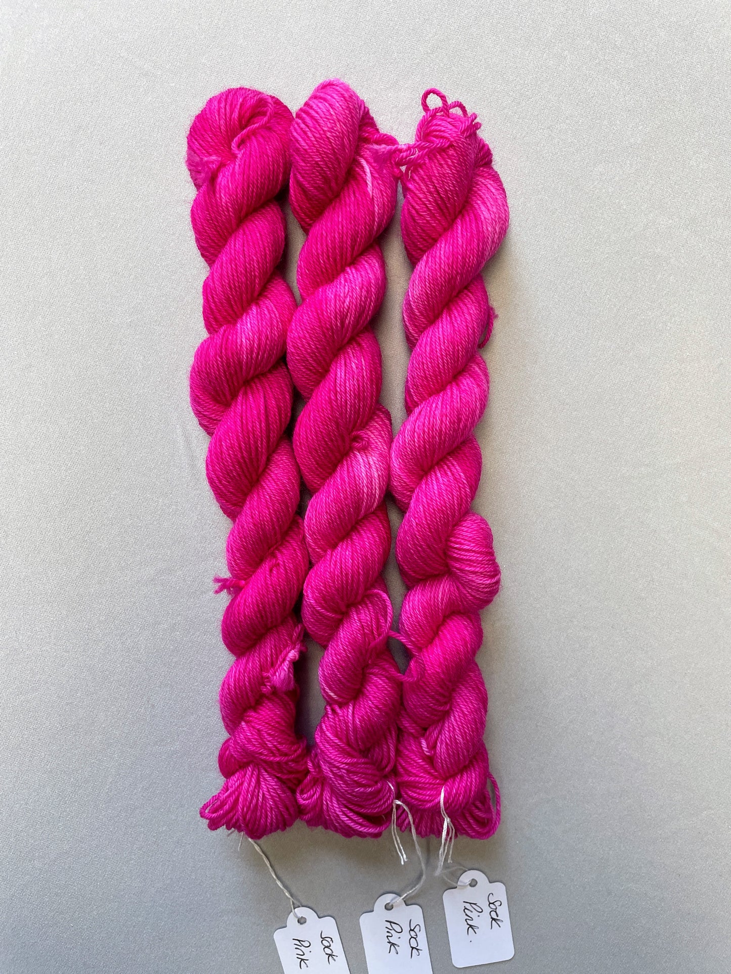 Zoomed in shot of 20g sock weight mini skeins in colourway Pink. A semi-solid colourway in a bright pink shade. 