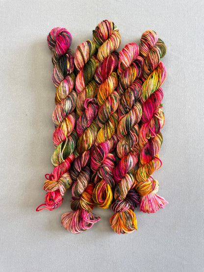 Full shot of 20g sock mini skeins in colourway Punk Rocker. An undyed yarn base with layers of Neon sprinkles in Yellow, Pink, Green and Black. This colourway glows under U.V. light. 