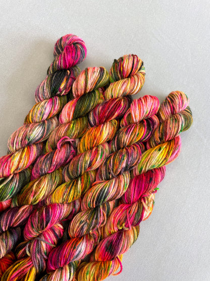 Close up shot of 20g sock mini skeins in colourway Punk Rocker. An undyed yarn base with layers of Neon sprinkles in Yellow, Pink, Green and Black. This colourway glows under U.V. light. 