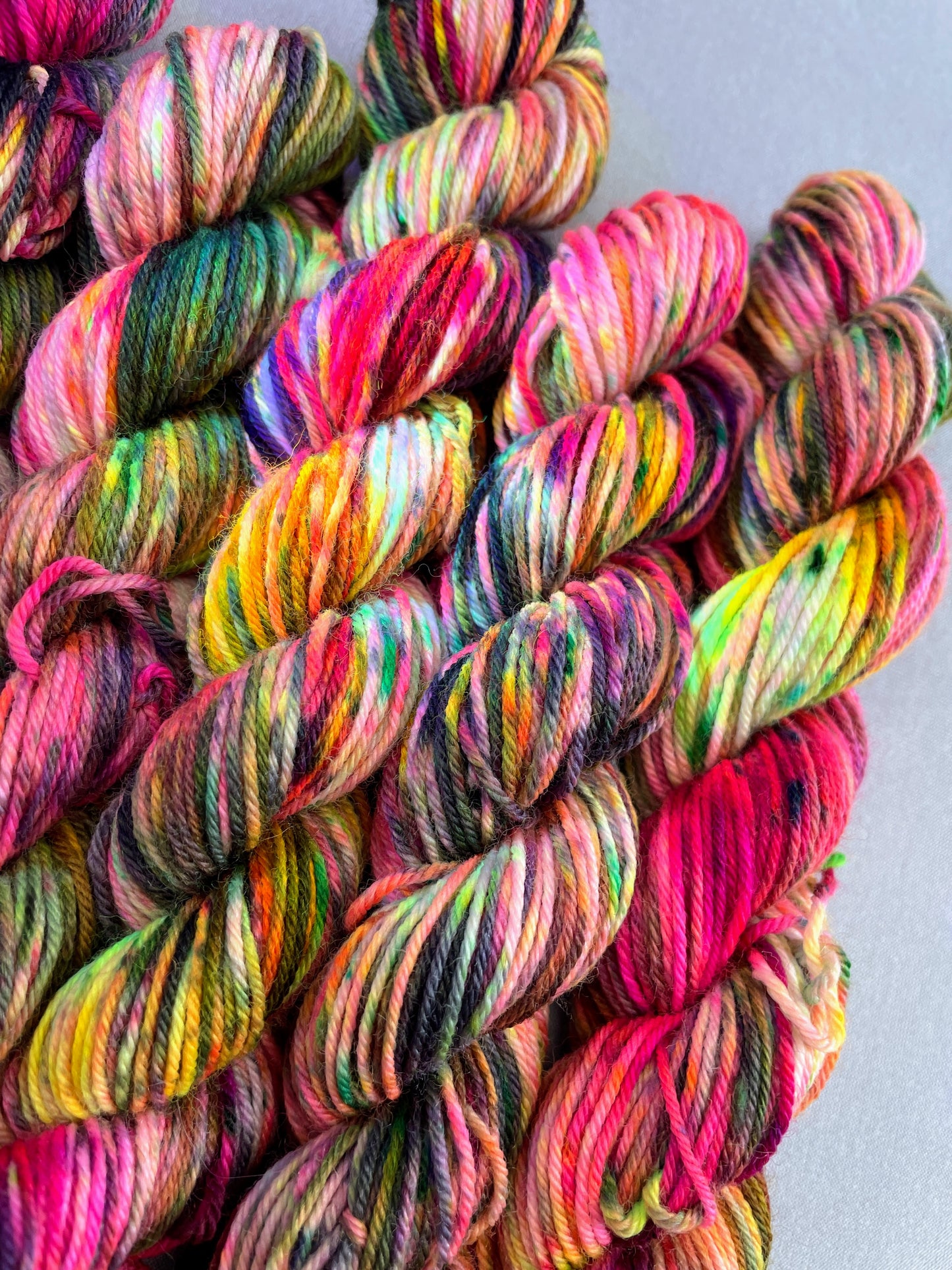 Close up shot of 20g sock mini skeins in colourway Punk Rocker. An undyed yarn base with layers of Neon sprinkles in Yellow, Pink, Green and Black. This photo shows the yarn speckles glowing under U.V. blue light.