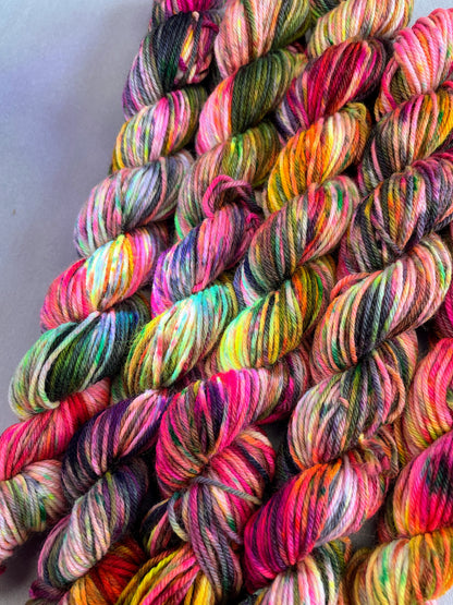 Close up shot of 20g sock mini skeins in colourway Punk Rocker. An undyed yarn base with layers of Neon sprinkles in Yellow, Pink, Green and Black. This photo shows the yarn speckles glowing under U.V. blue light.