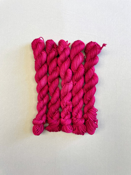 Full shot of 20g sock weight mini skeins in semi-solid colourway Raspberry, an intense, deep pink. Photographed on a light grey background.