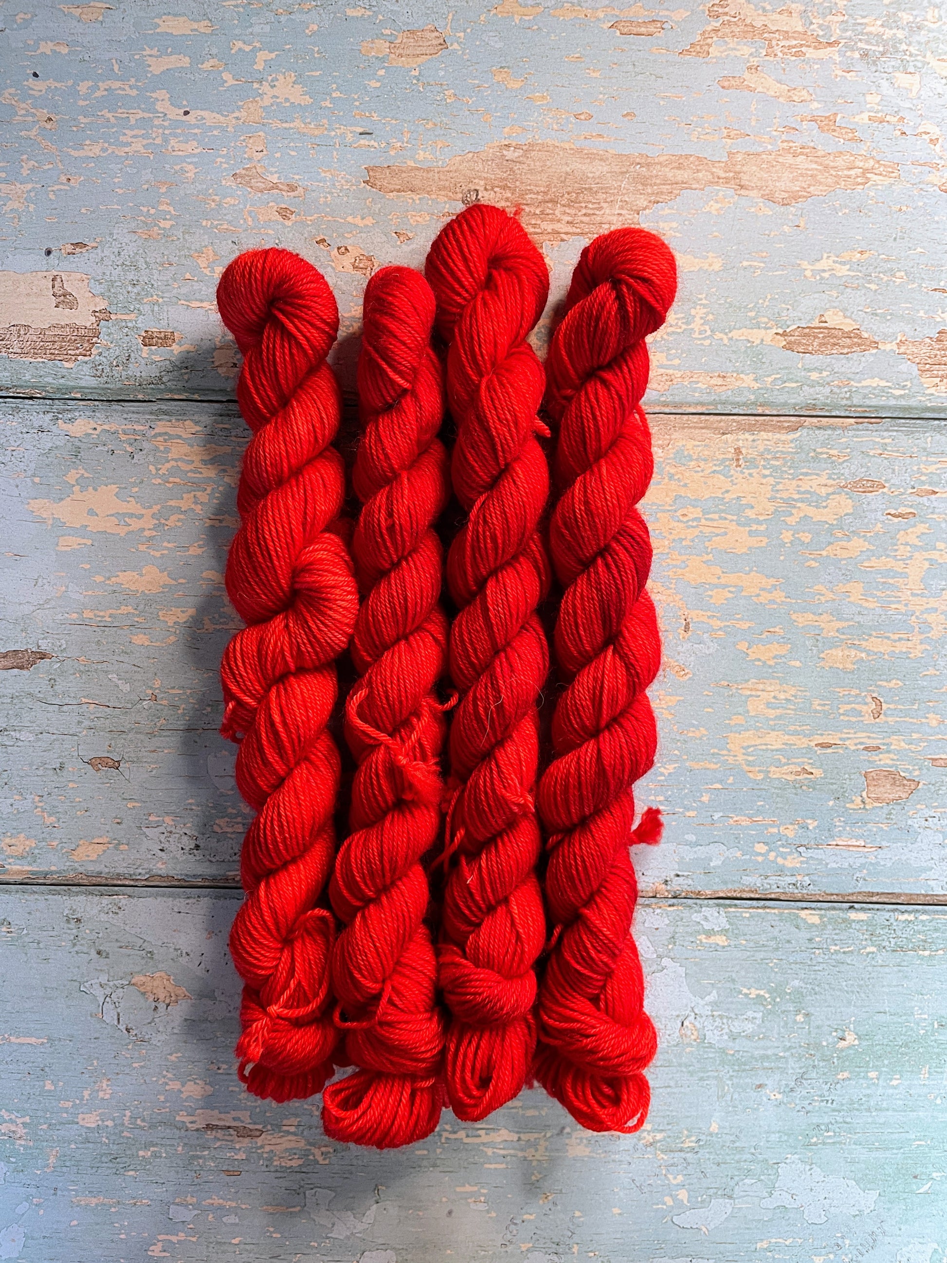 Full shot of 20g sock weight mini skeins in semi-solid colourway Ruby. This colourway is bright red. 