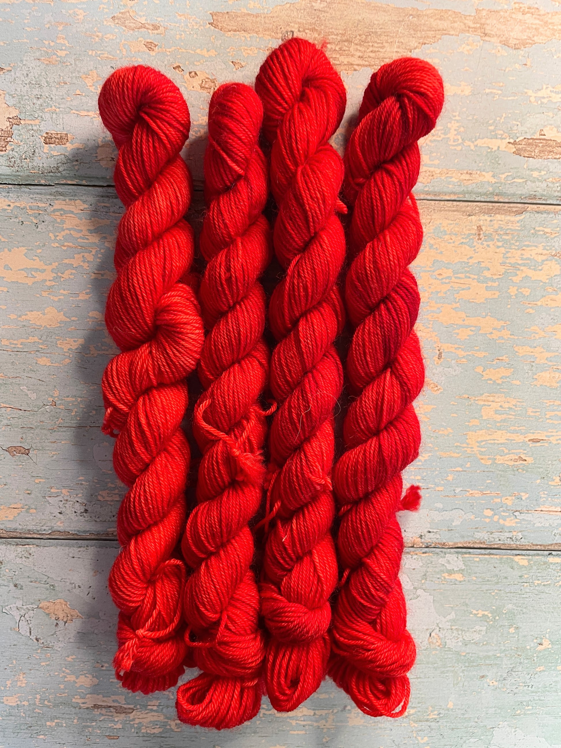 Zoomed in shot of 20g sock weight mini skeins in semi-solid colourway Ruby. This colourway is bright red. 