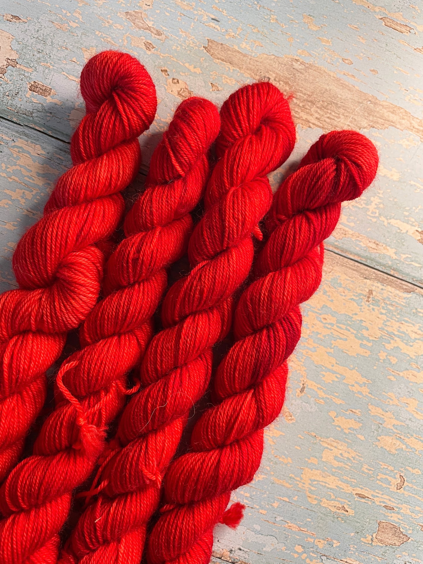 Close up shot of 20g sock weight mini skeins in semi-solid colourway Ruby. This colourway is bright red. 