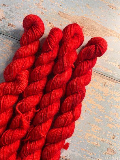 Close up shot of 20g sock weight mini skeins in semi-solid colourway Ruby. This colourway is bright red. 