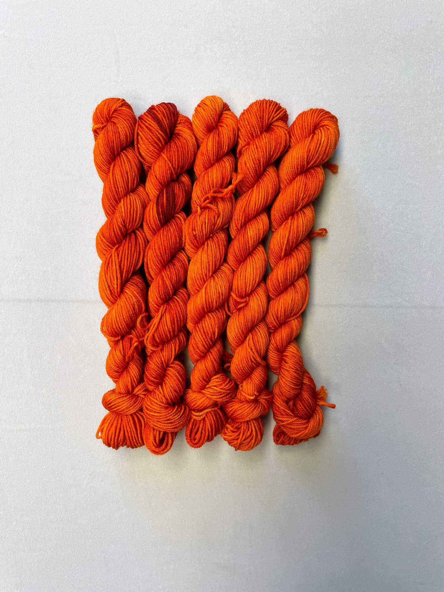 Full shot of 20g sock weight mini skeins in semi-solid colourway Saffron, a deep and intense orange colourway.