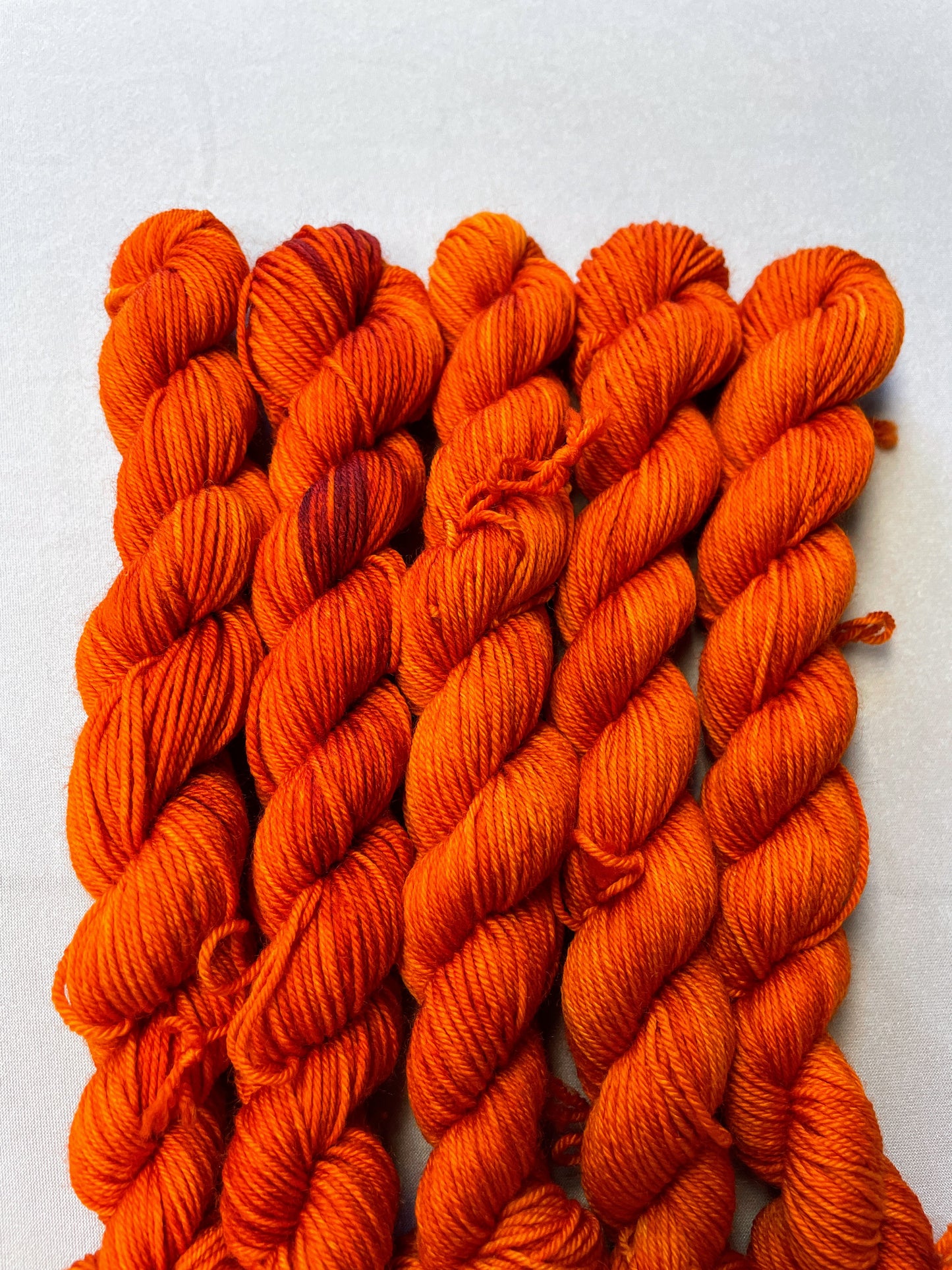 Close up shot of 20g sock weight mini skeins in semi-solid colourway Saffron, a deep and intense orange colourway.