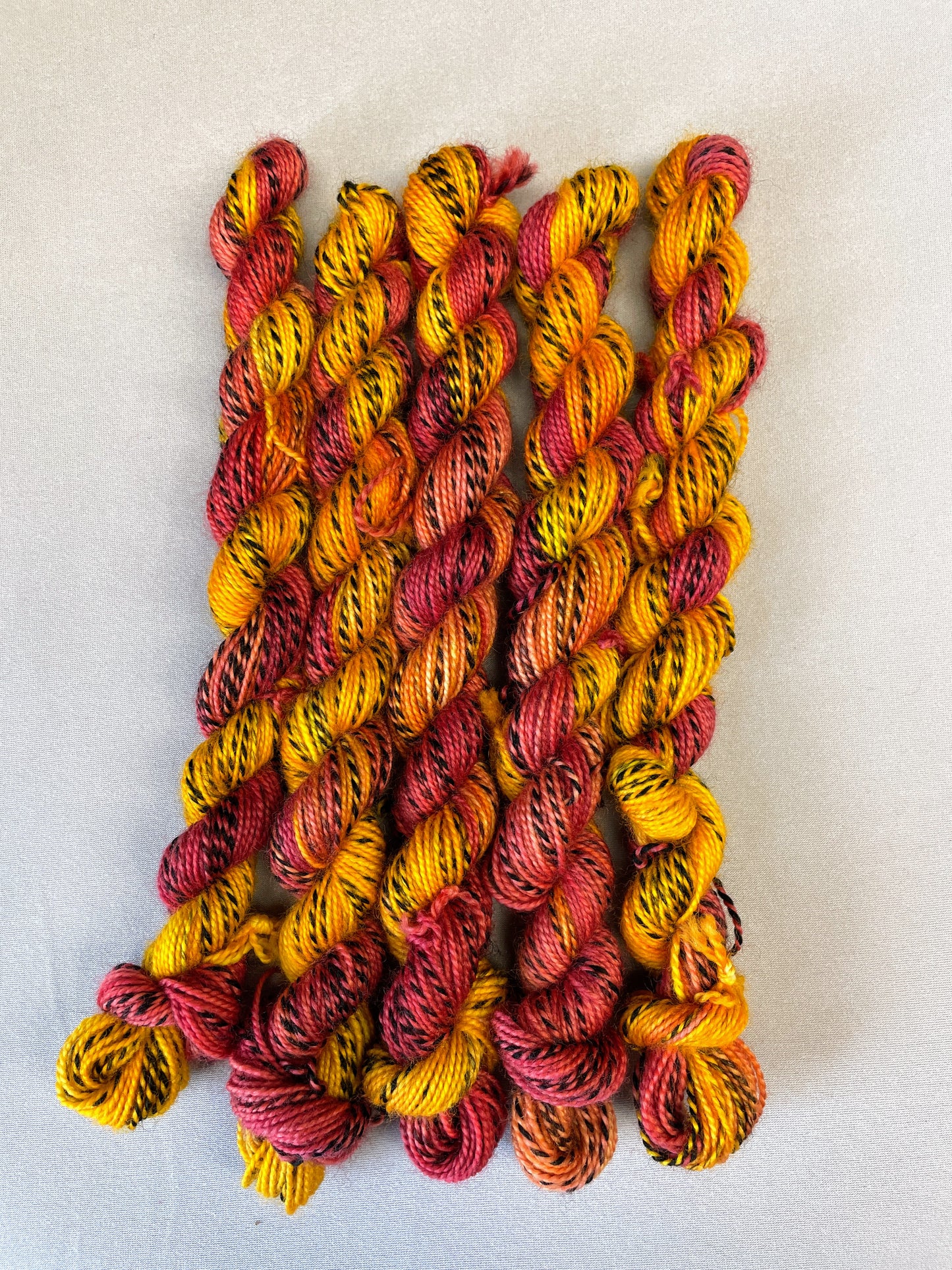 Hand-dyed Yarn
5 x 20g twisted, Zebra Sock mini skeins in colourway Phoenix, photographed on light grey background. This colourway is full of tones of Golden Poppy, Ruby Red and Saffron with the black and white strip running through it. 