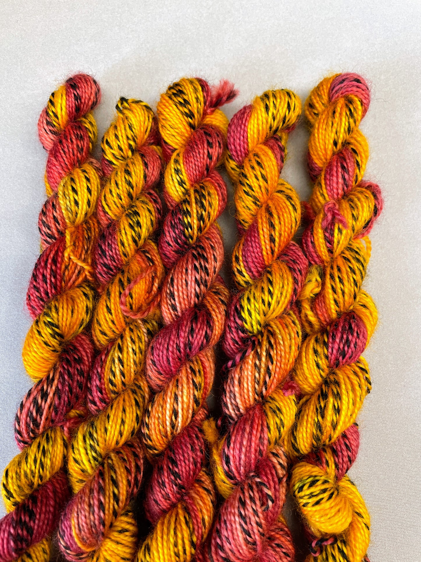 Hand-dyed Yarn
5 x 20g twisted, Zebra Sock mini skeins in colourway Phoenix, photographed on light grey background. This colourway is full of tones of Golden Poppy, Ruby Red and Saffron with the black and white strip running through it. 